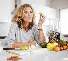 Woman smiling while snacking on fruit in kitchen