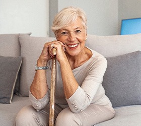 Woman in beige on couch smiling leaning on walking cane