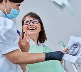 Woman smiling with dentist while reviewing X-ray