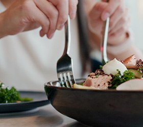 Hands scooping salad onto plate from bowl with forks