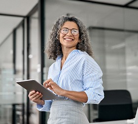 Woman in striped shirt in office holding tablet device smiling