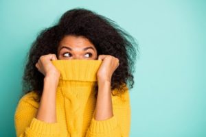 Woman covering her mouth with the neck of her yellow sweater