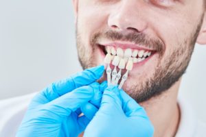 Dentist holding shade guide next to man’s teeth