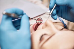 Facial closeup of a dentist examining a woman's mouth with blue gloves on